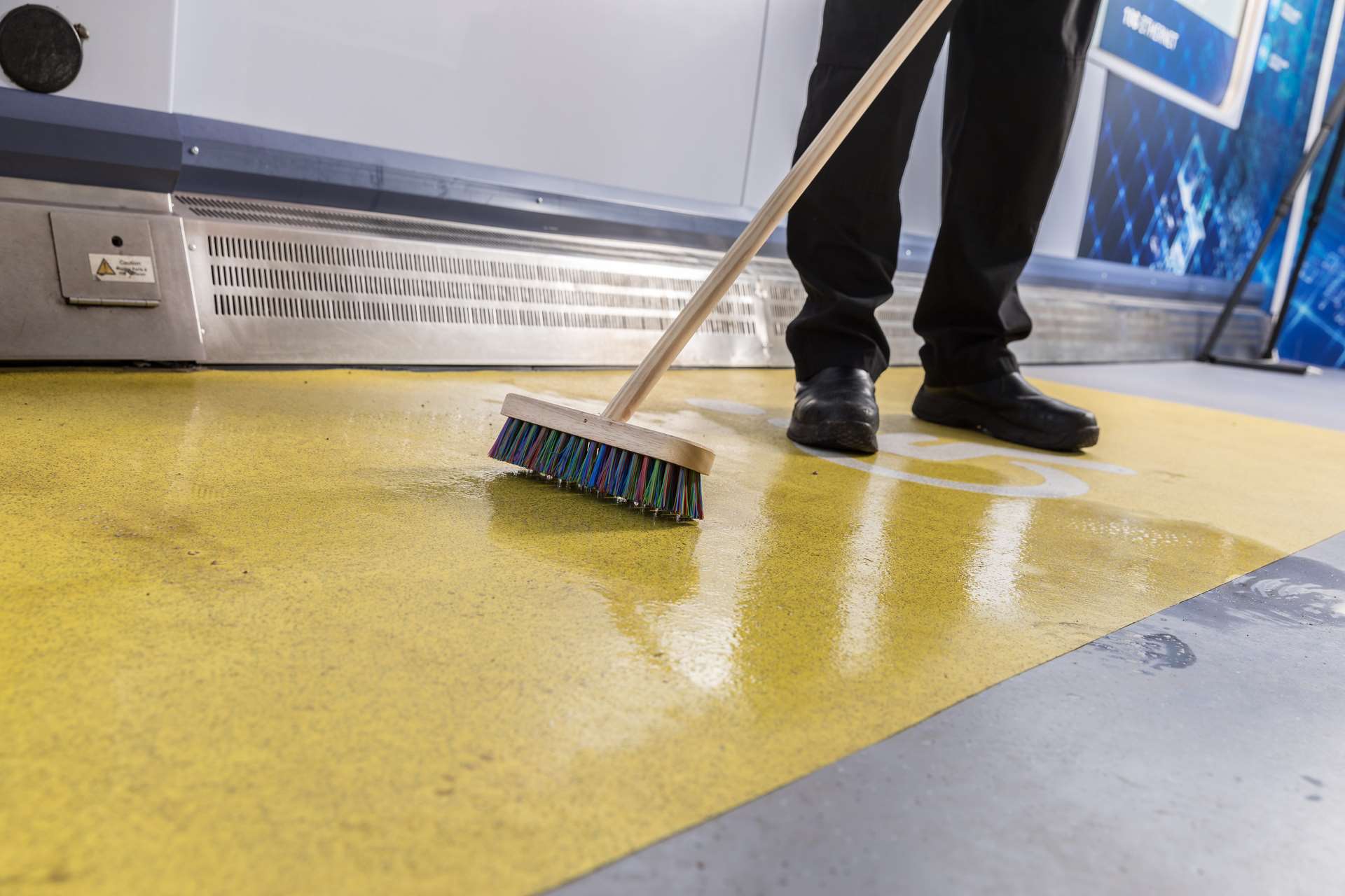 An Autoglym engineer performing a scrub with a deck brush as part of a deep clean on Altro Transflor Tungsten and Altro Transflor Motus