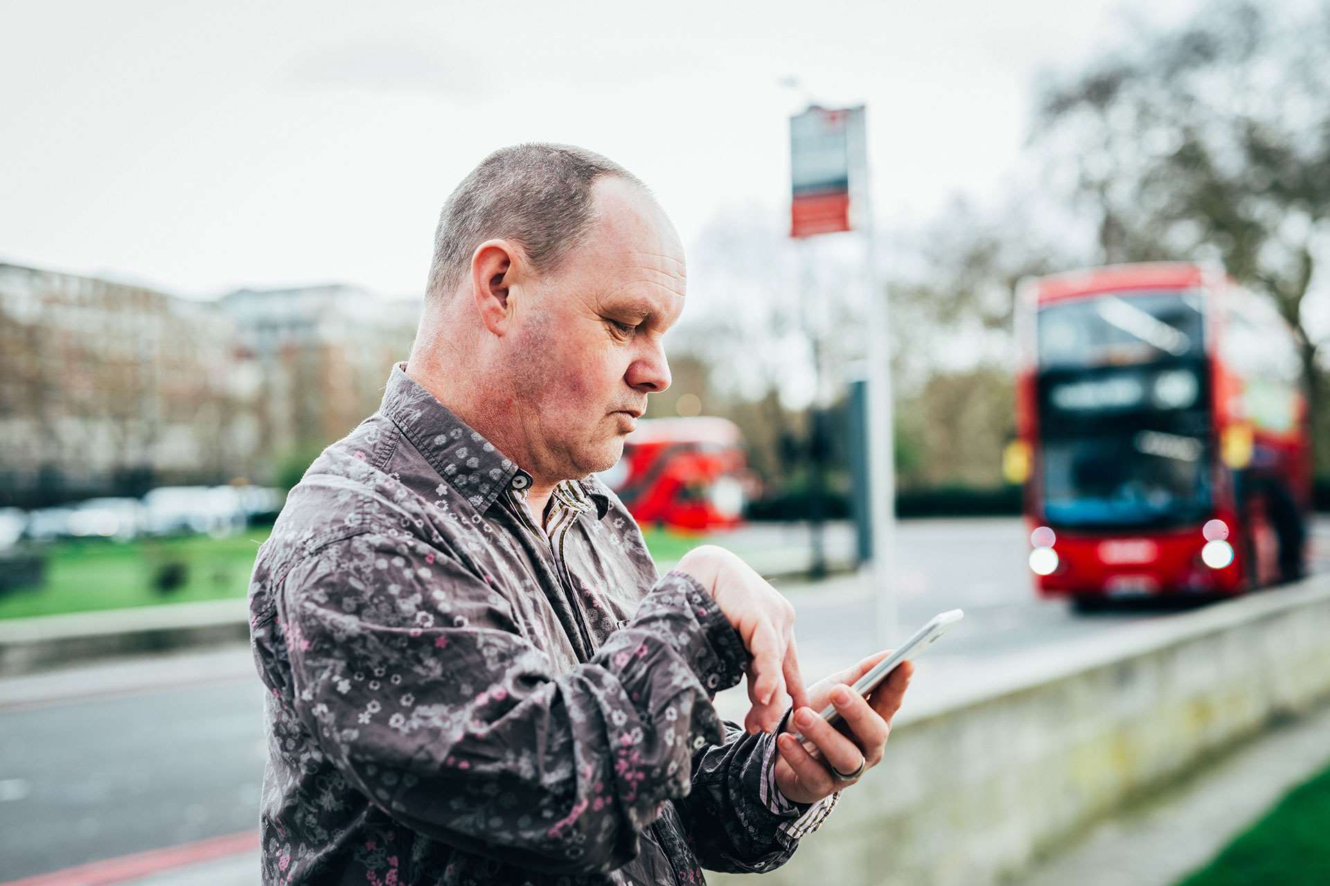 A man with a accessibility difficulties using a smartphone to check bus times while standing at a bus stop.