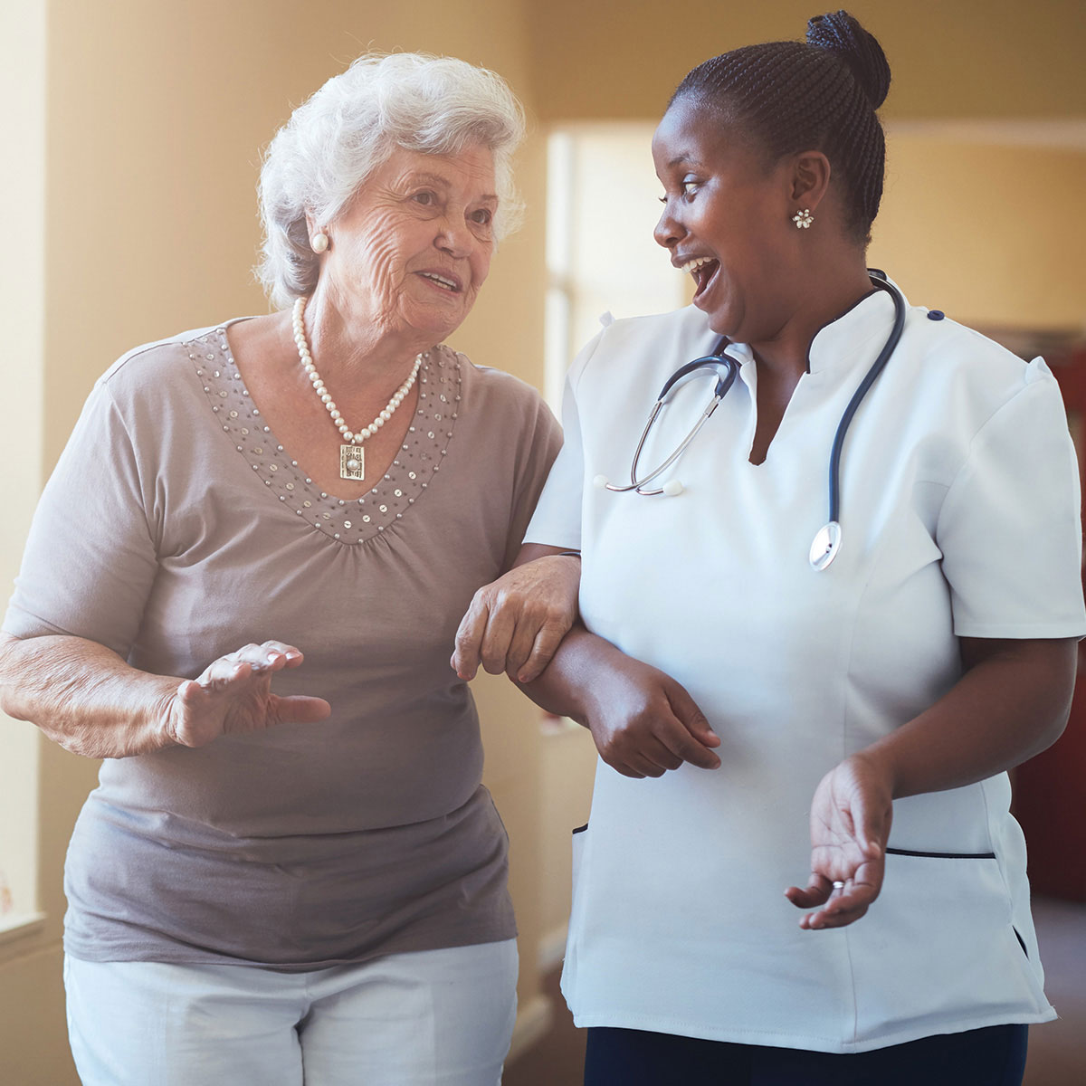 A senior lady walking arm-in-arm with a member of care home staff